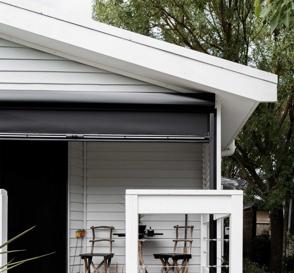 Slim headbox motorized patio screen tucked under the eave of a white weatherboard home