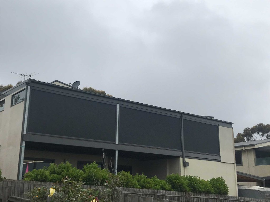 Three-bay motorized zip-track screens enclosing a second-storey balcony on an overcast day