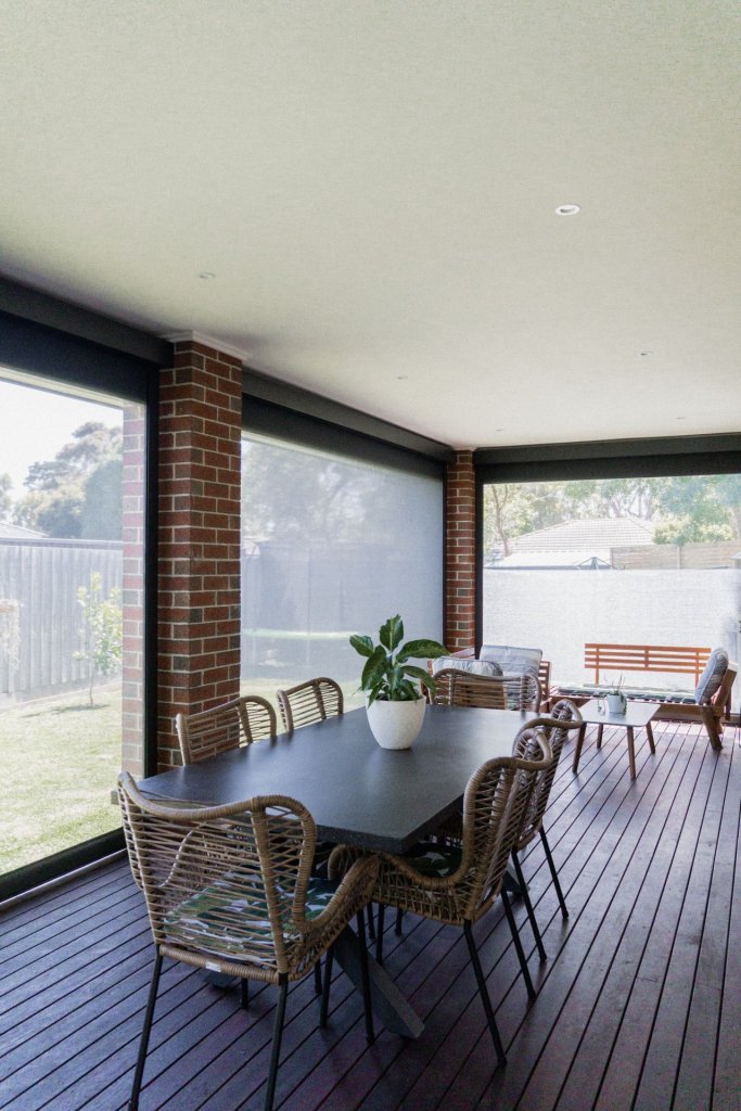 Interior view from a covered patio looking out through lowered zip-track screens to a backyard
