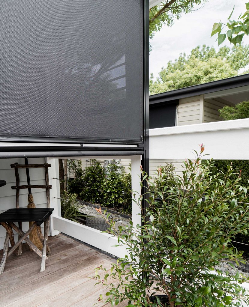 Open-weave motorized patio screen lowered beside a planted deck preserving the view through