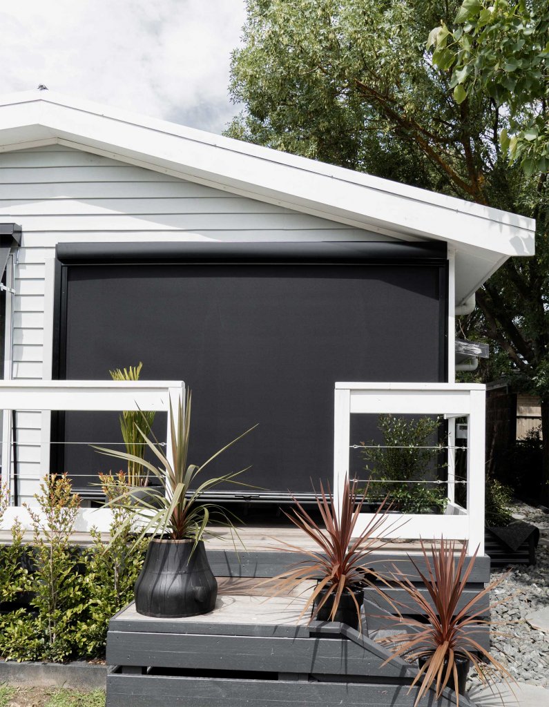Wide black motorized patio screen fully closed across the gable end of a weatherboard cottage