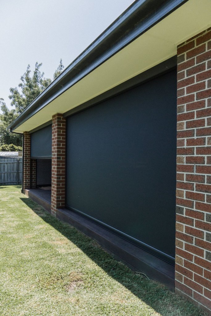 Close-up of charcoal motorized screens between brick columns on a covered patio
