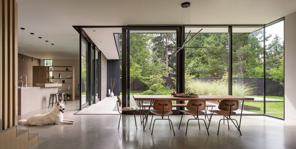 Modern dining area with corner sliding glass walls and garden views